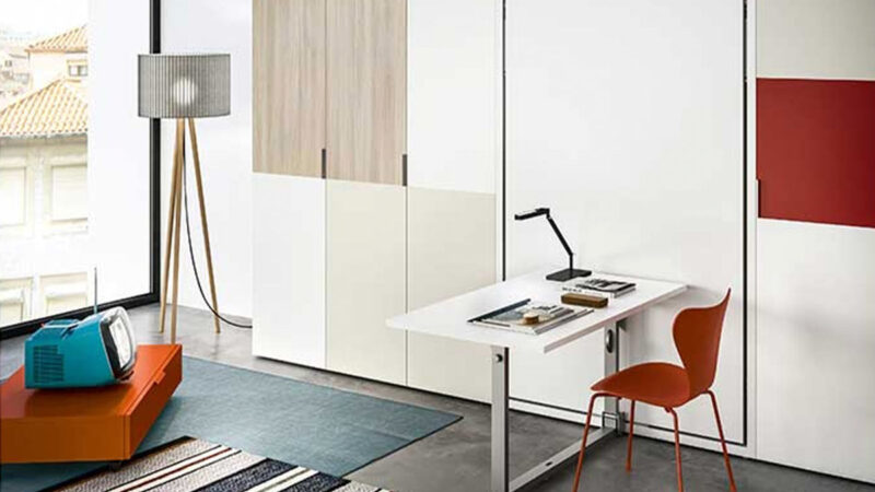 Cama abatible vertical con mesa funcional, diseño elegante y somier de lamas que optimiza el espacio en lofts y apartamentos pequeños.