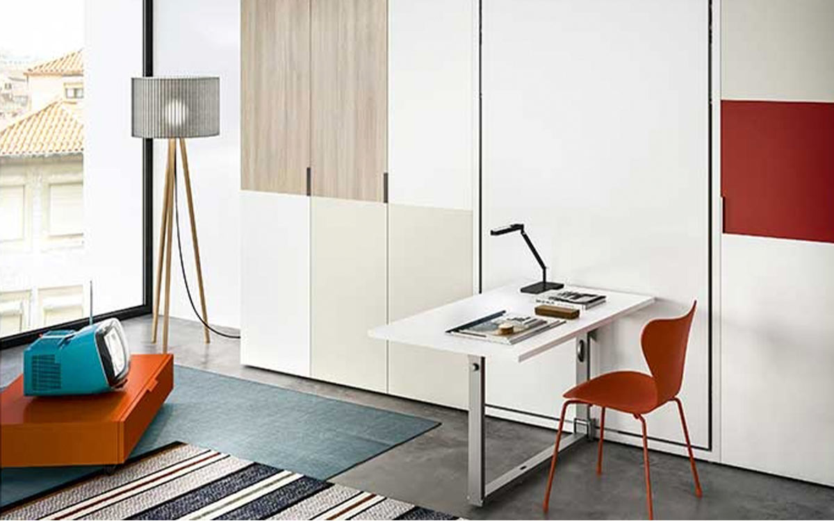 Cama abatible vertical con mesa funcional, diseño elegante y somier de lamas que optimiza el espacio en lofts y apartamentos pequeños.