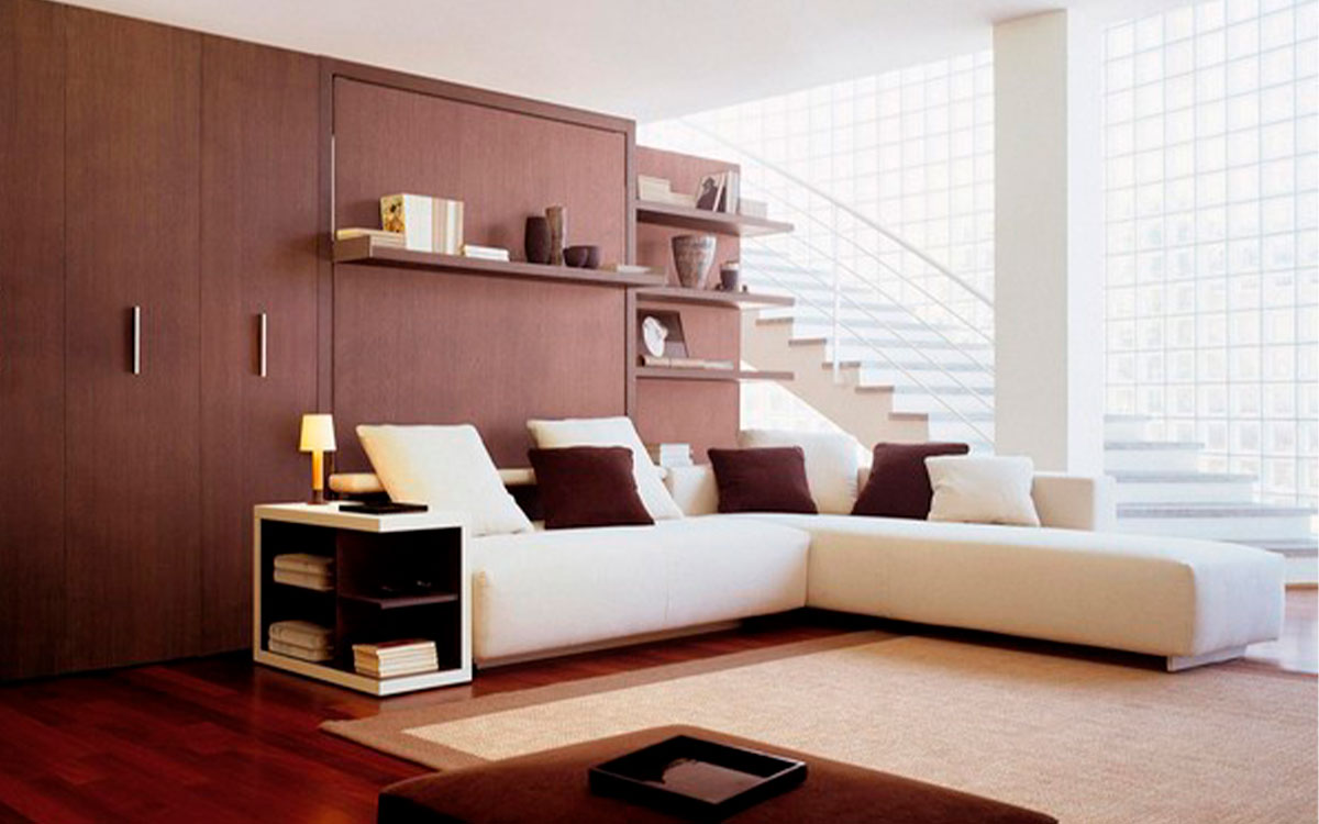 Cama abatible de matrimonio con sofá rinconero y almacenaje inferior integrado.