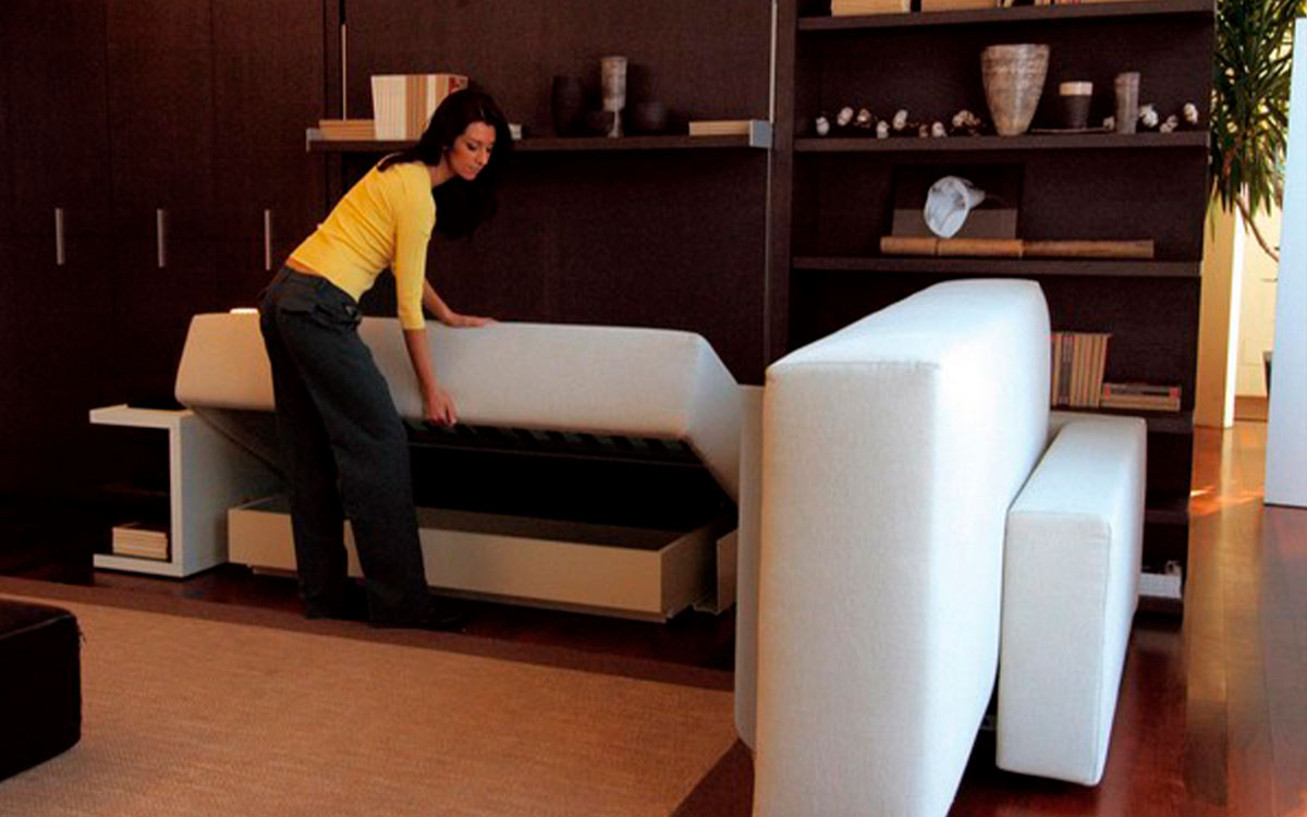 Cama abatible de matrimonio con sofá rinconero y almacenaje inferior integrado.