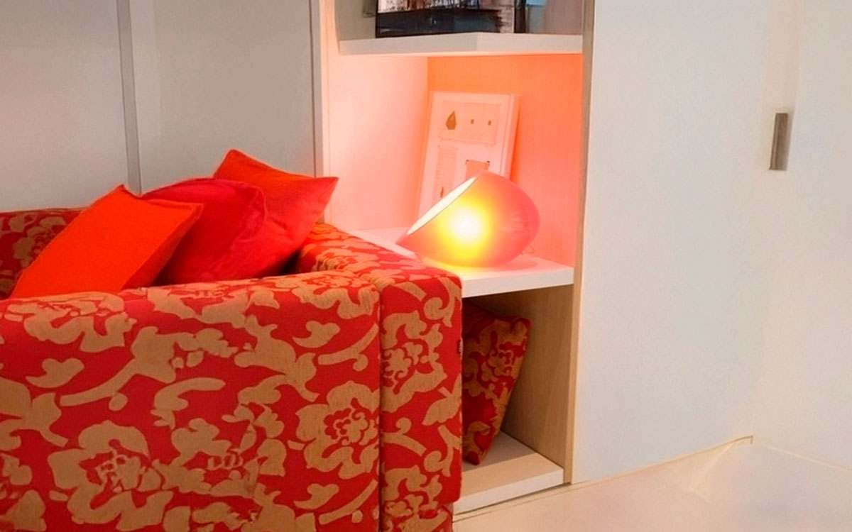 Mueble cama abatible de matrimonio con sofá diván delantero y estantería integrada.